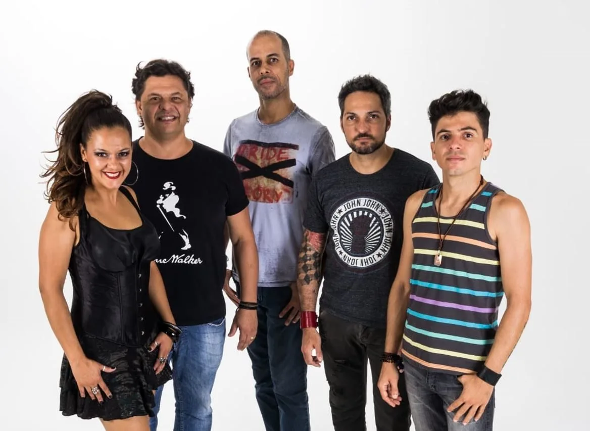 Integrantes da Banda Putzgrilla posam em estúdio com fundo branco, exibindo estilo moderno e expressões confiantes. A vocalista aparece à esquerda com look preto estilizado, enquanto os demais membros vestem camisetas e regatas despojadas, destacando a diversidade visual e a energia pop-rock do grupo mineiro.