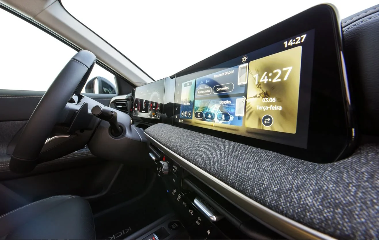 Painel digital do novo Nissan Kicks 2025 em destaque, com duas telas integradas de 12,3 polegadas para instrumentos e multimídia, interface personalizável com comandos de conectividade e climatização visíveis, acabamento em tecido no painel frontal e detalhes em preto brilhante, evidenciando a modernidade e sofisticação do interior do SUV compacto brasileiro.
