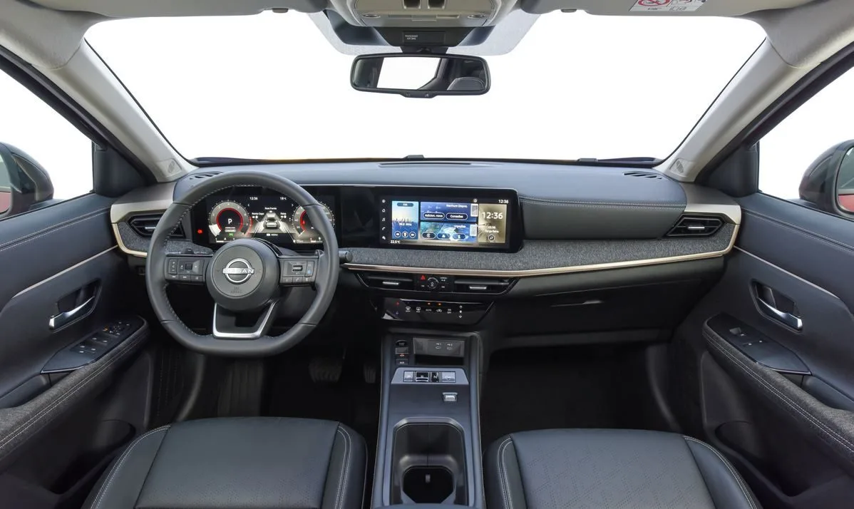 Interior do novo Nissan Kicks 2025 visto a partir do banco traseiro, destacando o painel digital com telas de 12,3 polegadas integradas para instrumentos e multimídia, acabamento sofisticado em tecido, volante multifuncional com comandos intuitivos e console central com seletor eletrônico e-Shifter, reforçando o padrão premium e tecnológico do SUV compacto nacional.