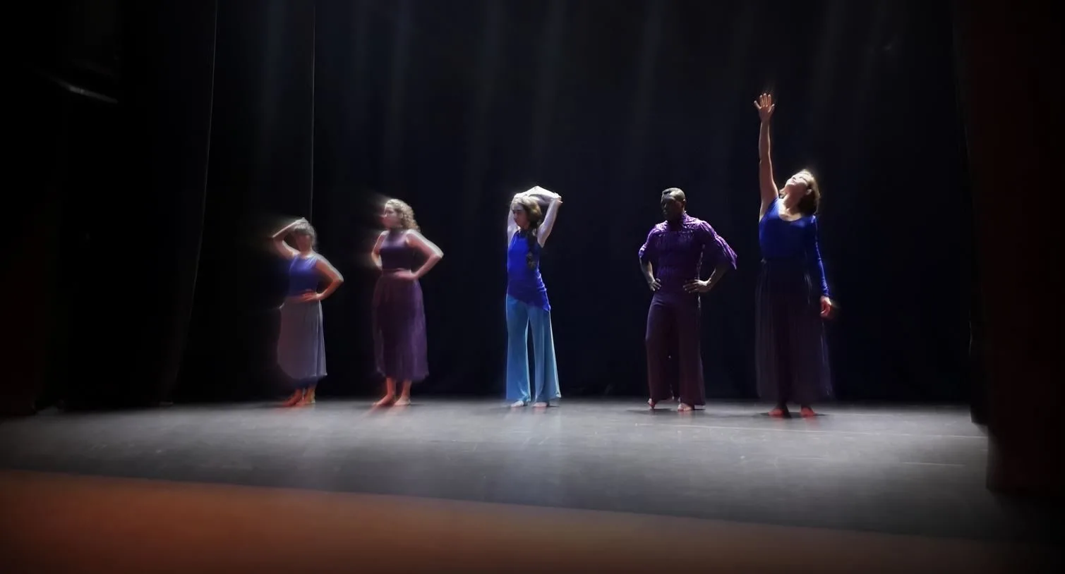 Formandos do curso de Dança do Arena da Cultura em cena no palco do Teatro Marília, em performance do espetáculo “Vazante”, com gestos expressivos e iluminação cênica marcante.