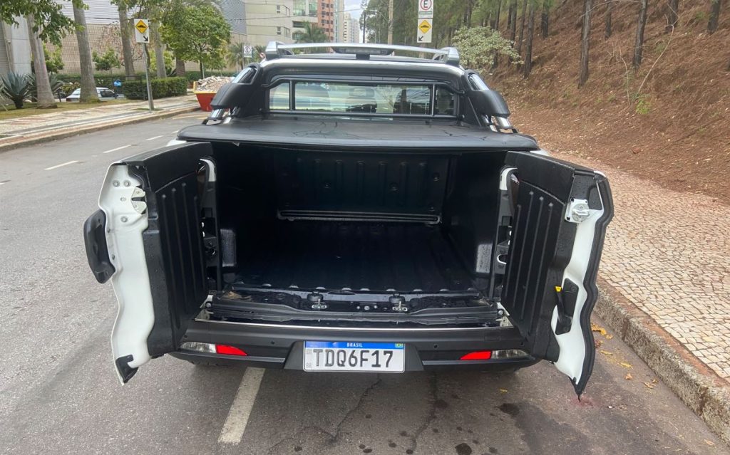 Vista traseira da Fiat Toro Ranch 2.2 Turbodiesel com a caçamba aberta. As portas bipartidas revelam um compartimento espaçoso e revestido, ideal para transporte de cargas. A imagem destaca também os detalhes do para-choque, lanternas e o design robusto da traseira.
