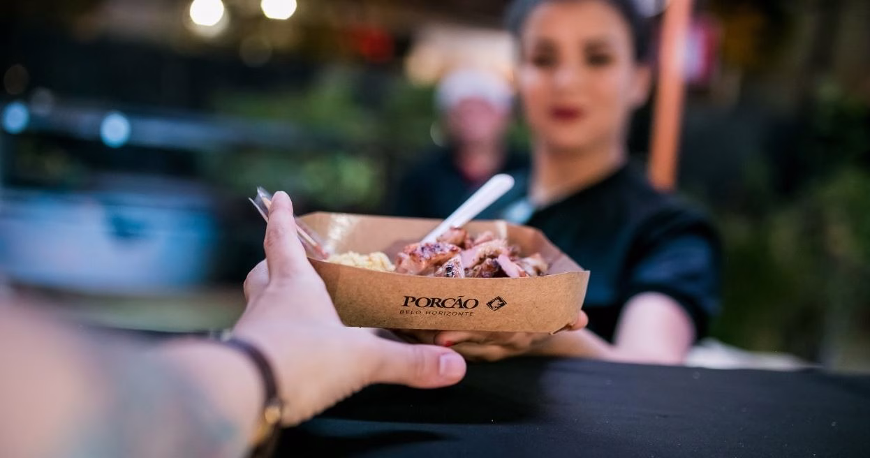 Cliente recebe porção de carne assada com farofa servida em embalagem personalizada da Churrascaria Porcão, durante evento gastronômico em BH.
