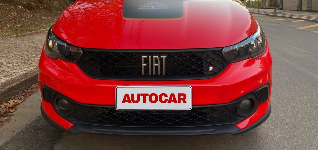 Detalhe frontal do Fiat Argo Trekking 2026 em vermelho, exibindo grade com logo Fiat escurecido, faróis Full-LED e capô com grafismo central exclusivo.