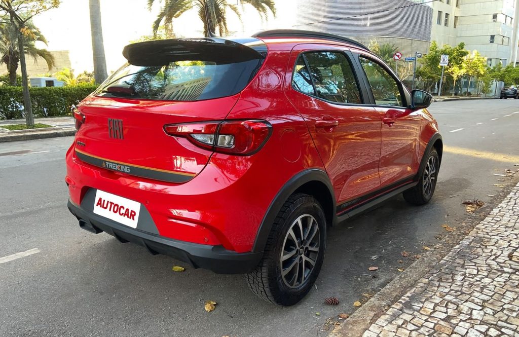 Vista traseira do Fiat Argo Trekking 2026 na cor vermelha, com lanternas escurecidas, faixa preta com o emblema "Trekking" e rodas de liga-leve, estacionado em rua urbana com calçada de pedras portuguesas.