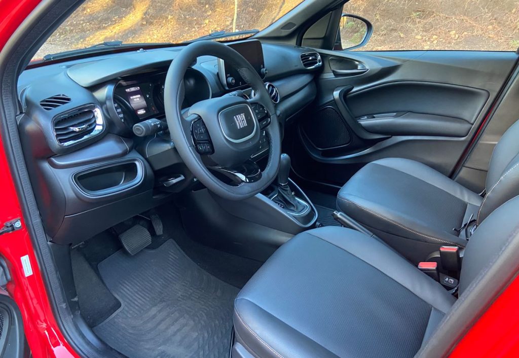 Interior do Fiat Argo Trekking 2026 com acabamento escurecido, volante multifuncional, central multimídia flutuante e câmbio automático CVT.