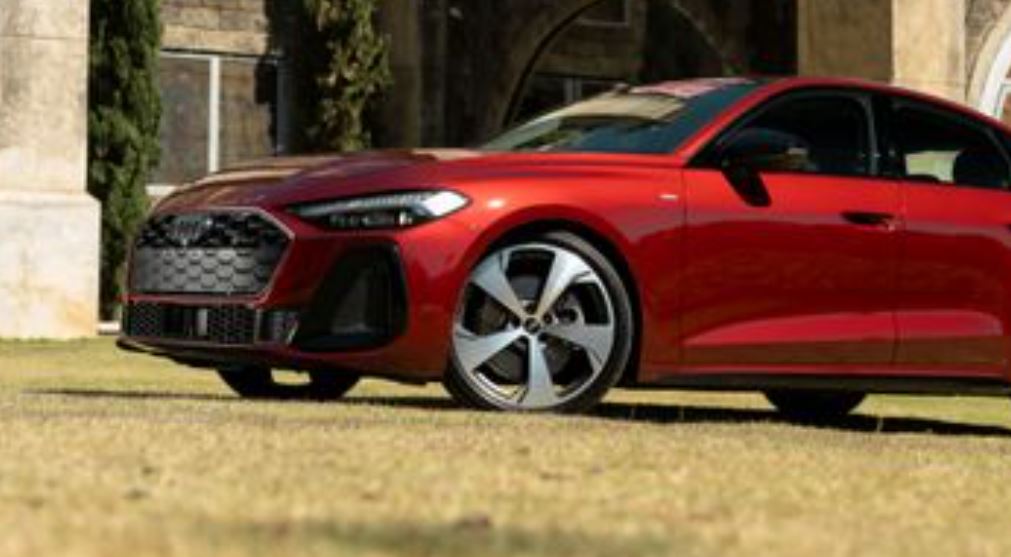 Vista lateral e frontal do Audi A5 2025 em vermelho, com destaque para as rodas Audi Sport de 20”, faróis LED e grade esportiva.