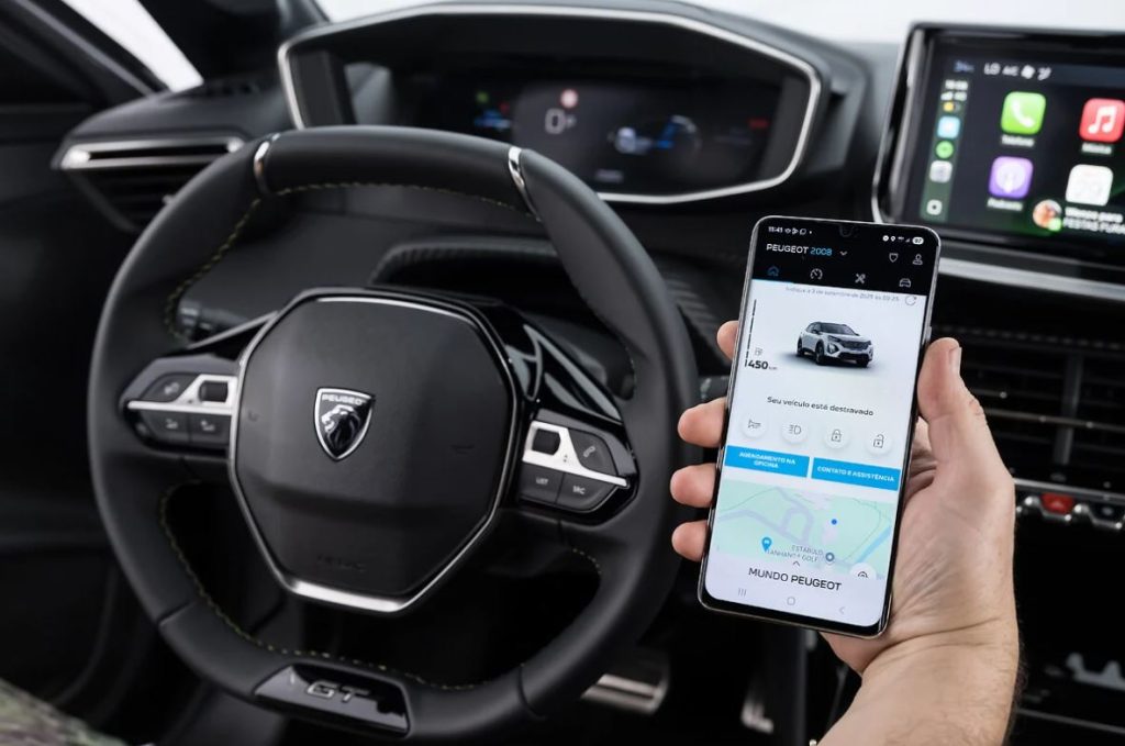 Volante do Peugeot 2008 GT híbrido com painel digital ao fundo e mão segurando smartphone exibindo o app MyPeugeot com funções remotas.