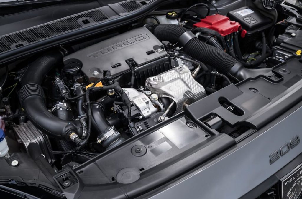Detalhe do motor turbo do Peugeot 208 GT híbrido, destacando o layout compacto, componentes elétricos e sistema de indução forçada.