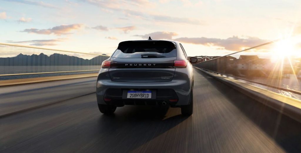 Traseira do Peugeot 208 GT híbrido em movimento sobre ponte, destacando o design moderno e iluminação traseira em LED.