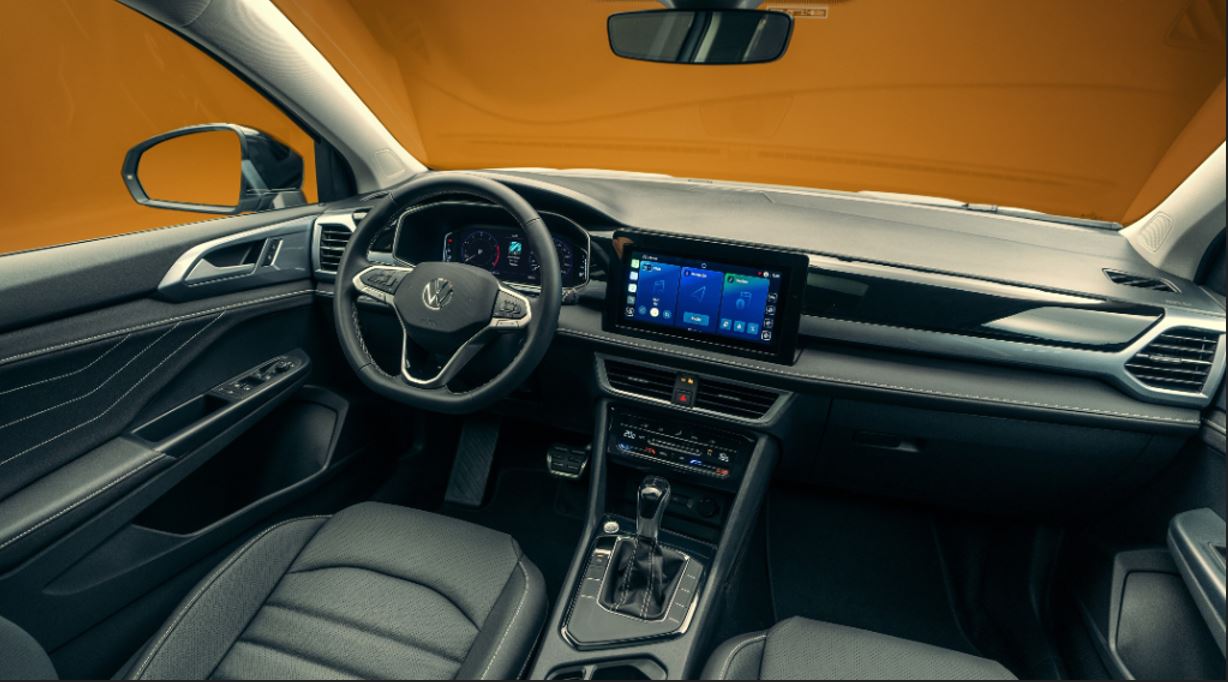 Interior do Novo Volkswagen Taos 2026 com painel digital Active Info Display, central multimídia flutuante VW Play Connect, ar-condicionado dual zone, acabamento premium com costuras contrastantes e volante multifuncional com comandos físicos.
