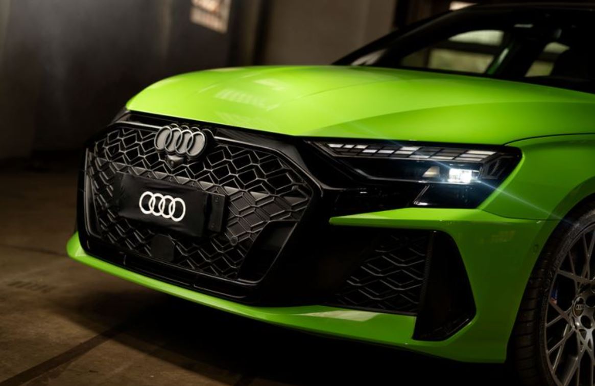Close da grade frontal do Audi RS 3 Sedan em Verde Kyalami, evidenciando o padrão hexagonal esportivo e os faróis Matrix LED acesos.