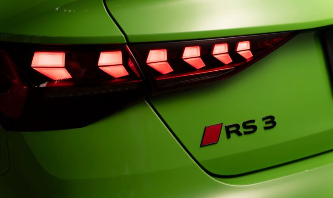 Detalhe da lanterna traseira em LED do Audi RS 3 Sedan iluminada, com elementos geométricos e emblema RS 3 sobre a carroceria Verde Kyalami.
