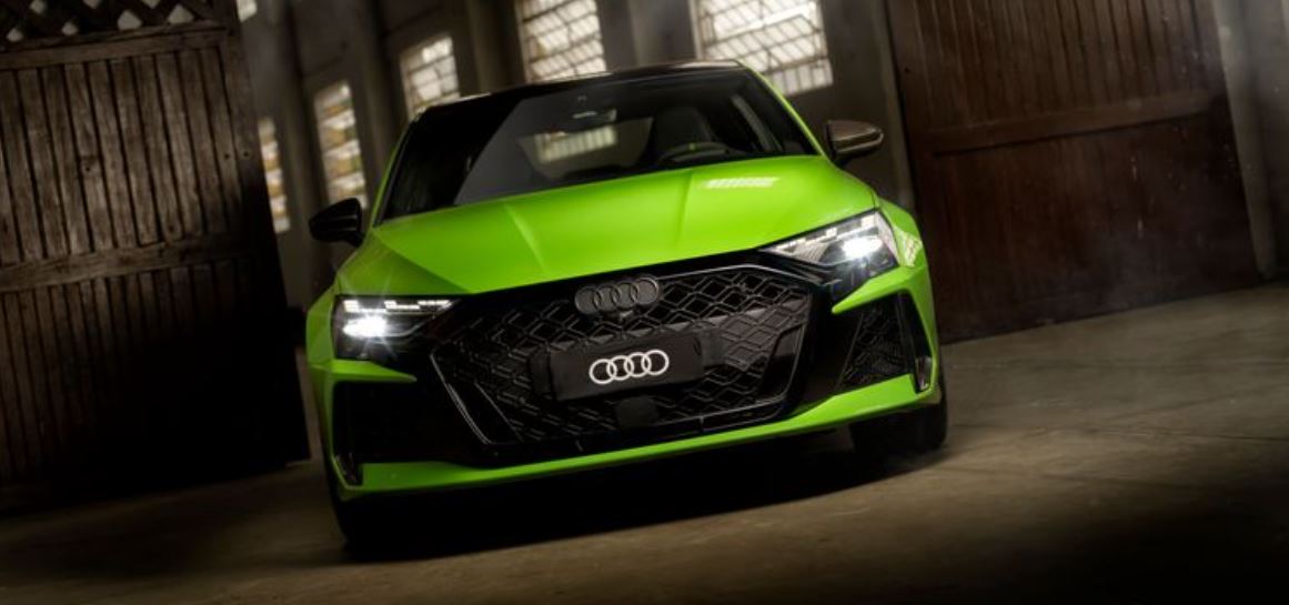Frente do Audi RS 3 Sedan na cor Verde Kyalami em ambiente fechado, destacando a assinatura luminosa dos faróis Matrix LED e a grade Singleframe em preto brilhante.