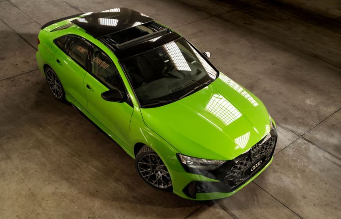 Vista superior do Audi RS 3 Sedan em Verde Kyalami, com teto panorâmico escurecido e rodas esportivas de liga leve, estacionado em ambiente fechado.