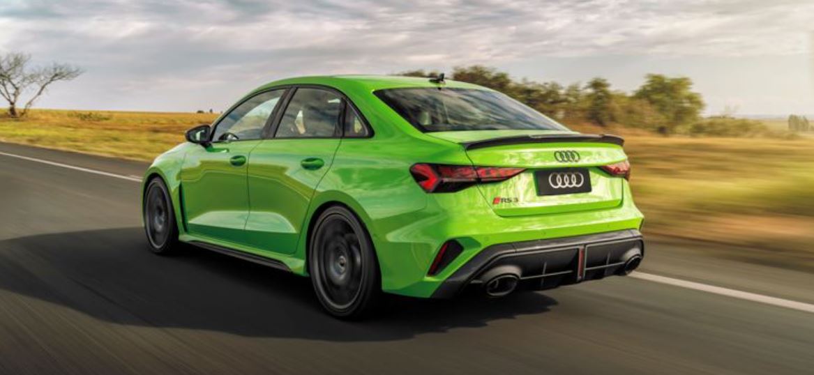 Vista traseira do Audi RS 3 Sedan em movimento, na cor Verde Kyalami, destacando difusor esportivo, escape duplo e aerofólio integrado.