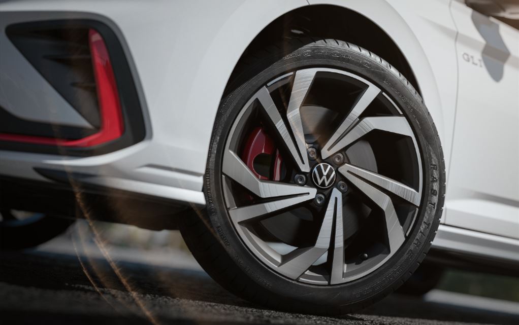 Detalhe da roda de liga leve aro 18 do Volkswagen Jetta GLI 2026, com acabamento diamantado em preto e prata, pinça de freio vermelha e pneu de perfil esportivo, reforçando o design agressivo e a identidade visual do modelo.