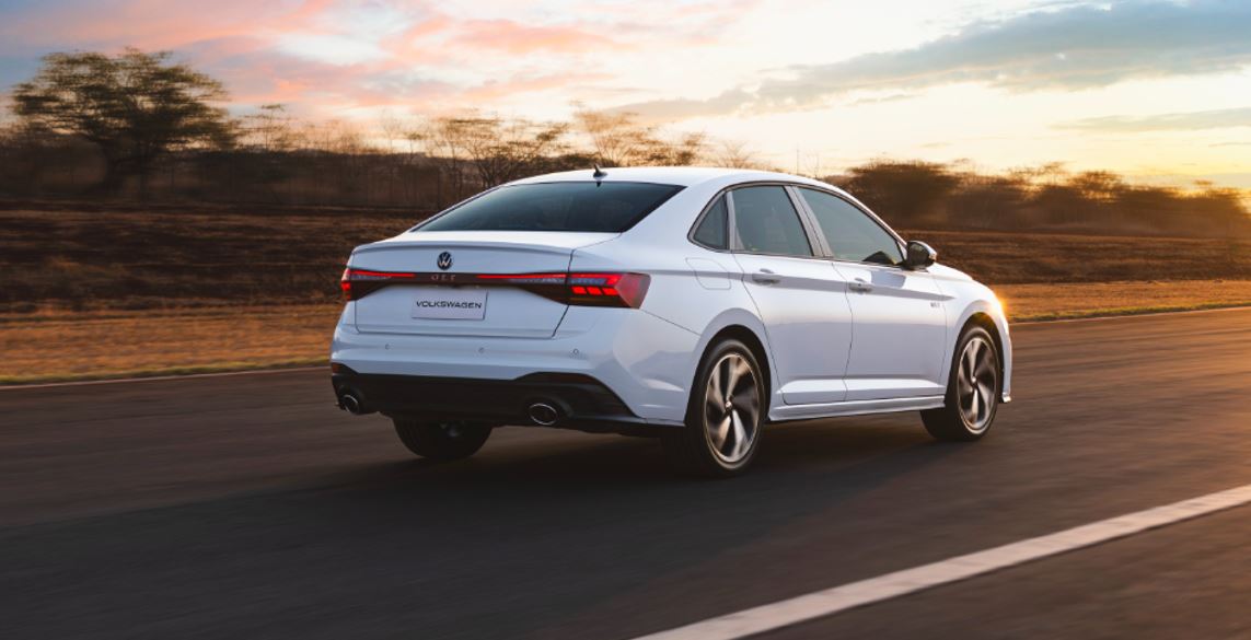 Traseira do Volkswagen Jetta GLI 2026 na cor branco puro, em movimento, com lanternas em LED conectadas por faixa luminosa, dupla saída de escapamento e detalhes esportivos sob o pôr do sol.