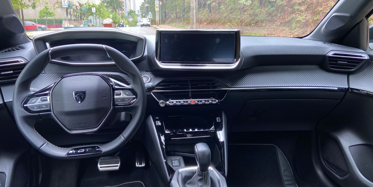 Painel do Peugeot 208 GT híbrido com volante esportivo GT, central multimídia flutuante, teclas estilo piano e acabamento em fibra de carbono.