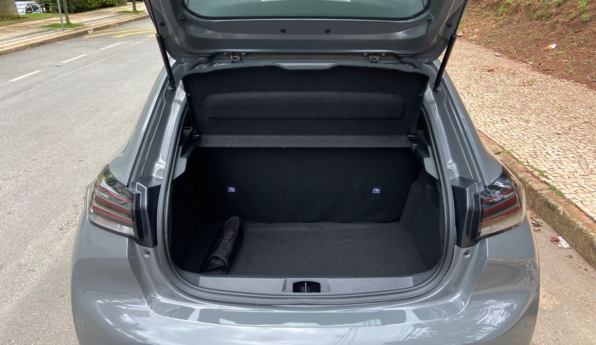 Porta-malas aberto do Peugeot 208 GT híbrido, com acabamento interno em carpete preto e bom espaço de bagagem.