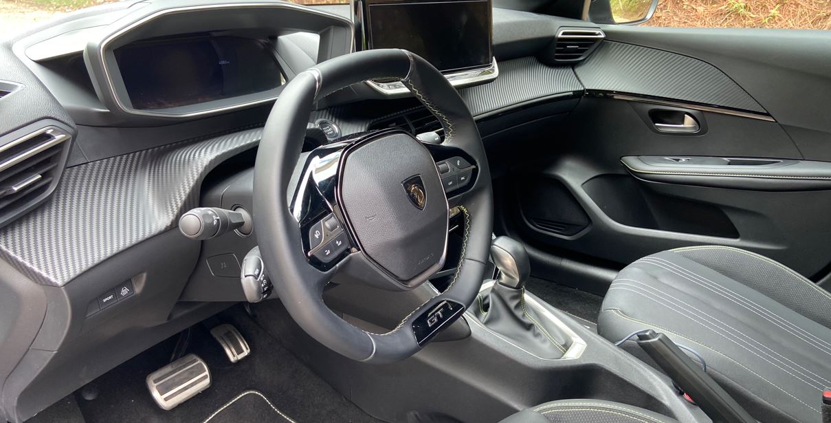 Detalhe do volante esportivo GT em couro com costuras contrastantes, painel elevado e acabamentos sofisticados do Peugeot 208 híbrido.