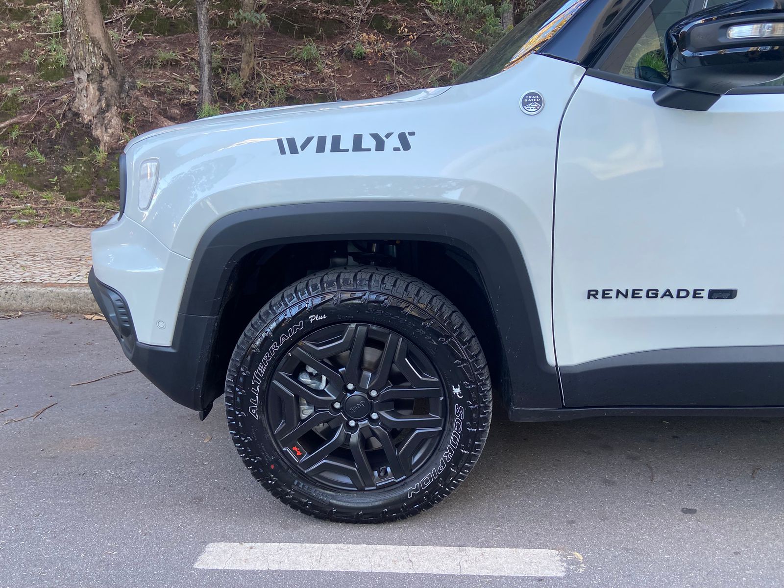 Detalhe da lateral dianteira do Jeep Renegade Willys 10 Anos, com logotipos “WILLYS” e “RENEGADE”, roda preta e pneu Scorpion All Terrain Plus.