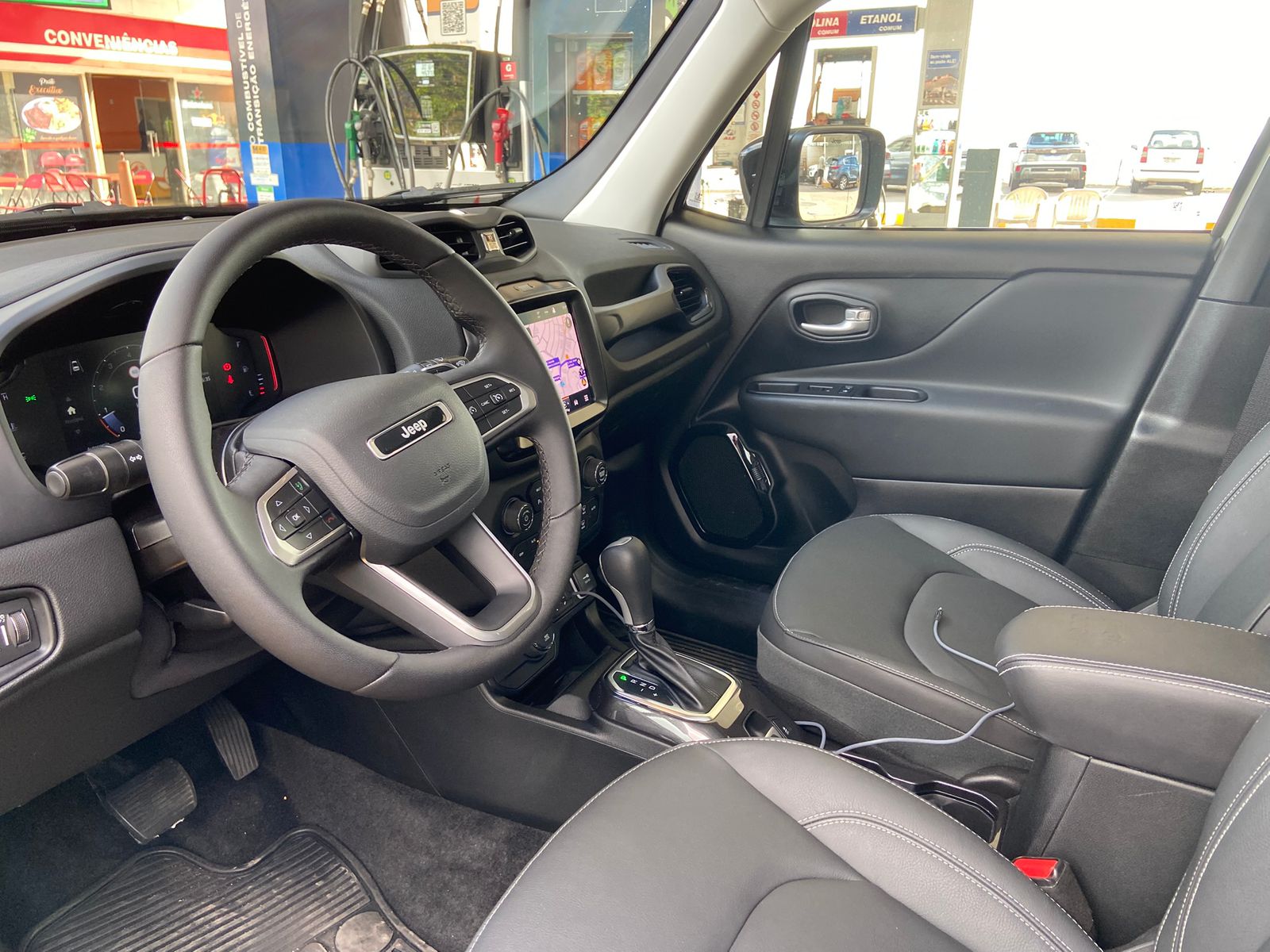 Interior do Jeep Renegade Willys 10 Anos com volante multifuncional, central multimídia com GPS, câmbio automático e bancos em couro preto.