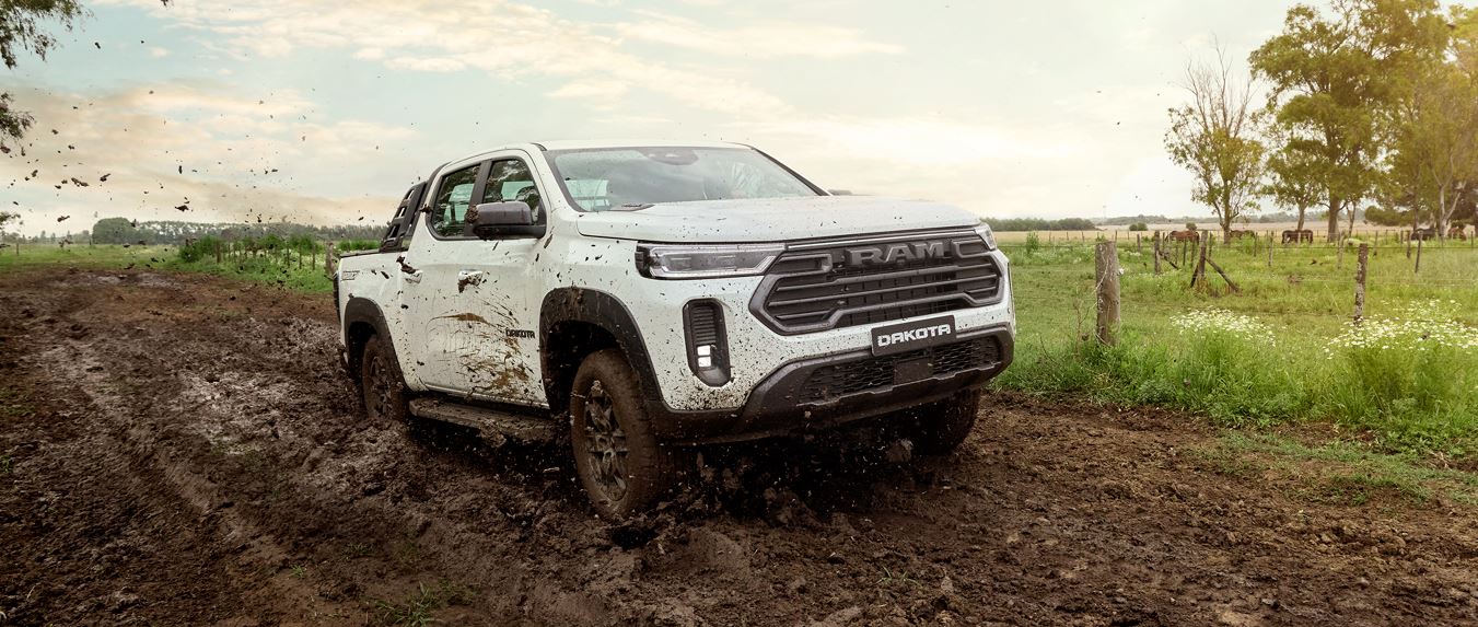 Picape Ram Dakota 2026 em teste off-road, avançando em terreno lamacento, com destaque para a tração 4x4, frente robusta e suspensão elevada.